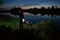 Night fishing, fisherman with a fishing rod standing on the shore of lake