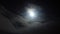 During the night, a full moon majestically rises above the sea, its brilliance obscured by drifting clouds, casting a