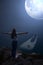 Night landscape of Cape Roca and Atlantic ocean in Portugal with a huge moon in the sky. A rear view of a girl standing on the