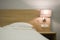 Night light at the head of the bed in the evening. Detail of still life of bedroom interior with bed, bedside table and lamp.