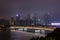 Night modern city with skyscrapers. Bridge over the river, city buildings glow at night. The sky in the clouds hides the building.