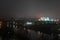 Night panorama of the big city at the foot of the river. Lots of colorful burning lights and street lighting. Top view of houses