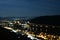 Night photo of the city through which the river flows, blurred background of the mountain along which the highway goes.