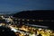 Night photo of the city through which the river flows, blurred background of the mountain along which the highway goes.