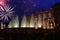 Night photo of the festive salute above the building of the opera and ballet theater and fountains with backlight.