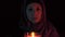 A night portrait of a witch casting spell over a red candle and making witchcraft, she moves a candle close up to the