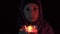 A night portrait of a witch casting spell over a red candle and making witchcraft, she moves a candle close up to the camera and