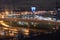 On night roads, cars drive over a bridge and a road junction. Urban cityscape