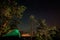 Night scene with illuminated camping tent, forest and starry sky