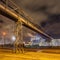 Night scene with illuminated petrochemical production plant and massive pipeline overpass