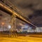 Night scene with illuminated petrochemical production plant and pipeline overpass,