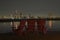 Night scene of wooden chairs at the waterfront lookout with a view of night lights of a cityscape.