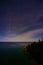 Night sky with whisps of soft pink clouds over Michigan lake and a cliff with a dark forest on the bottom right