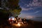 Night summer camping on shore. Group of young tourists around campfire near tent under evening sky