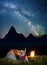 Night tent camping. Happy couple hikers sitting near tent and campfire and enjoying incredibly beautiful starry sky