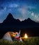 Night tent camping. Pair of tourists sitting near tent and campfire and looking to incredibly beautiful starry sky