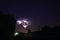 Night thunderstorm, distant illuminated cumulonimbus cloud and blue sky with stars, power lines and wires, trees