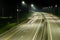 A night-time highway with long red and white stripes of light from the headlights of cars. There are streetlights at the edges of