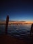 Night on the venice lagoon with mooring posts in silhouette city lights reflected in the sea and illuminated sunset sky