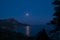 Night view of mount foros in Laspi Bay. A rocky mountain and fool moon above the sea. Moonwalk in the sea.