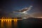 Night view of Piraeus harbor with moon partially hidden by clouds