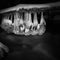 Night winter view to icicles on twigs and icy boulders above rapid stream. Reflections of head lamp in icicles. Black and white.