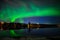 A nightscape view of aurora borealis with a city scape under starry clear sky and reflection from lake water