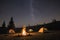 Nighttime camping under stars with glowing campfire and tents in a serene forest setting. Peaceful starry night concept.
