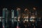 nighttime view of towering high-rises, with the lights shining and reflections shimmering in the water