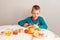 A nine-year-old boy sits at a table and cuts kiwi. The child prepares his own breakfast at home