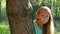 Nine years old girl hides behind a tree, gesturing silence. Close up