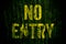 â€œNo Entryâ€ warning sign in yellow letters painted over dark grungy concrete wall with green moss.