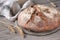 No knead handmade loaf on cutting board on wood with linen towel, spelt ears. German Bauernbrot means Rustic Farmers