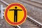 No trespassing sign on a train station with rail roads in the blurred background shows a black person symbol on an orange sign