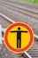 No trespassing sign on a train station with rail roads in the blurred background shows a black person symbol on an orange sign