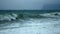 Noisy sea surf storm waves roll onto the shore and break into foam. Cloudy rocks on the horizon. Stunning seascape