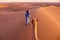 Nomadic tribesmen walking a camel through the Sahara Desert in Morocco at sunrise.