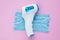 Non-contact infrared forehead thermometer and disposable surgical face mask with 3 layers of purifying, pink background. COVID