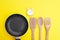 A non-stick skillet, a set of bamboo crockery and a white vintage clock on a bright yellow background.