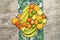 Non-stick tray full of washed bananas, tangerines, apples and limes with a top-down perspective on top of a tropical leaf tree tab