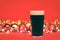 Nonik pint glass of dark beer or stout ale with christmas lights baubles and tinsel on red background