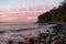 Noosa - peaceful waves, a rocky beach and pink clouds at sunset