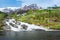 Nordic house on hill next to waterfall under blue sky