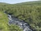 Northern landscape in Swedish Lapland with blue rapid stream of creek, green hills and birch tree forest at