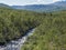 Northern landscape in Swedish Lapland with blue rapid stream of creek, green hills and birch tree forest at