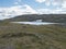 Northern landscape, tundra in Swedish Lapland with blue artic lake with reamains of melting snow cave, green hills and