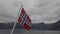 Norwegian flag hanging on the railing of the ship and waving above the water. Norvegian fjord with a flag. Ferry trip in