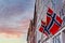 Norwegian flags waving in the wind on the wall of an old wooden house in Bergen against a beautiful sky at sunset