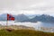 Norwegian national flag waiving in the wind on the top of Nonstinden peak with fjord in the background, Ballstad, Vestvagoy