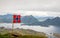 Norwegian national flag in the wind on the top of Nonstinden peak with fjord in the background, Ballstad, Vestvagoy Municipality,